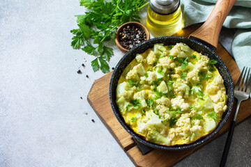 Healthy breakfast or diet lunch. Egg omelet with cauliflower in a cast-iron pan on a light stone table top. Copy space.