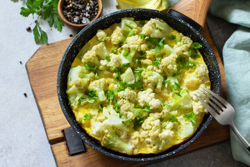 Healthy breakfast or diet lunch. Egg omelet with cauliflower in a cast-iron pan on a light stone table top.
