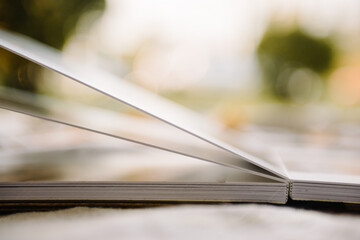 Open-page wedding photobook. The pages and their thickness are visible. Blurred background. Close-up