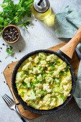 Healthy breakfast or diet lunch. Egg omelet with cauliflower in a cast-iron pan on a light stone table top.