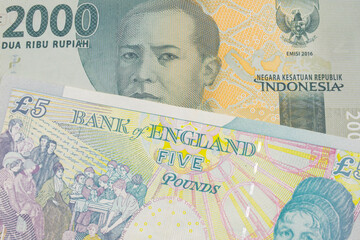 A macro image of a grey two thousand Indonesian rupiah bank note paired up with a colorful, five pound bank note from the United Kingdom.  Shot close up in macro.