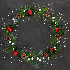 Abstract Christmas & winter wreath with holly, mistletoe, cedar cypress fir leaves, pine cones & silver balls on grunge grey background. Xmas & New Year composition. 