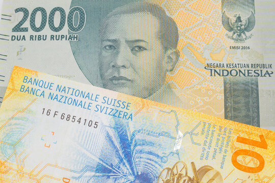 A macro image of a grey two thousand Indonesian rupiah bank note paired up with a yellow Swiss ten franc bill.  Shot close up in macro.