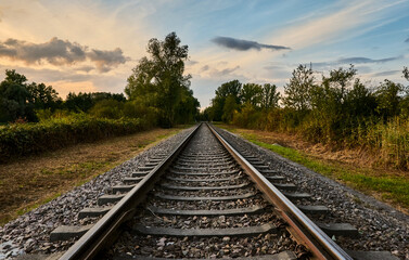 Fototapeta na wymiar Old railway tracks running through rural countryside with beautiful sunset sky