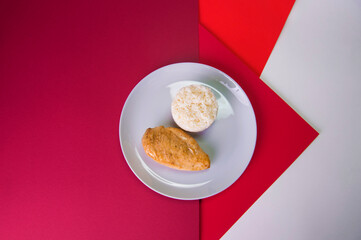 Top view of Tasty roasted chicken fillet on gray plate with boiled white rice served in culinary ring. Breakfast on colorful red background. Main and side dish in one plate.

