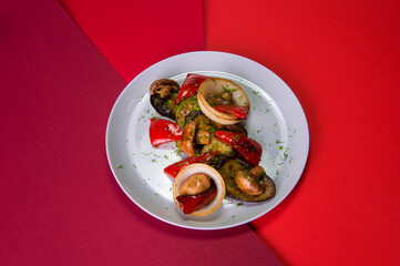 Side view of vegetarian dish. Mix of Grilled vegetables on gray plate. Colorful red background. Grilled mushrooms, bell pepper, onion, zucchini and eggplant served with fresh herb dill. Healthy food 
