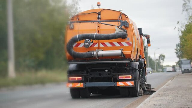 Orange machine clears the side of an asphalt with a sweeper