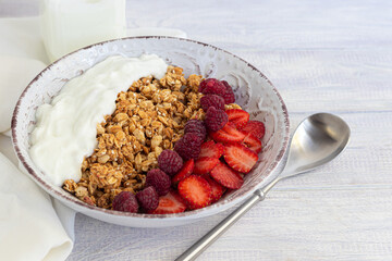 Homemade granola with strawberry chunks in a light plate and yogurt in a jar. On a light background. Vegetarian dish. Healthy breakfast.