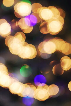 A Christmas tree photographed blurry so as to bring out the unfocused and thus circular shapes of its golden and multi-colored fairy lights.