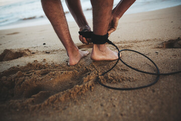 Man with surfboard getting ready to surf - strapping on leash