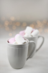 Hot winter drink with cocoa and marshmallows in mugs on wooden white background with Christmas garland. Top view.
