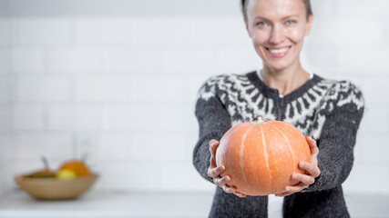 Beautiful woman in sweater with orange pumpkins in white kitchen, focus on pumpkin