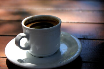 A white cup of black coffee on the wooden table in a summer cafe. Espresso. Coffee break.

