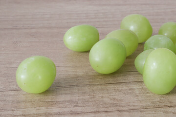 Scattered grapes beside bunch of fresh ripe rose grapes on wooden planks