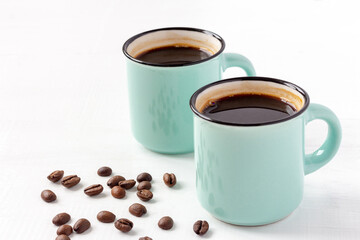 Two blue cups of fresh aromatic coffee with grains on white wooden background. Copy space