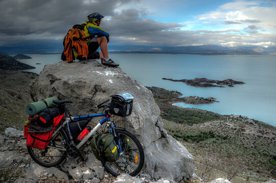 Young cyclist sitting on top of the rock and looking at big lake