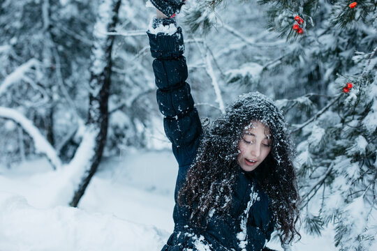 Preteenager girl with one arm up plays in the winter outdoors, snowflakes attached to her hair