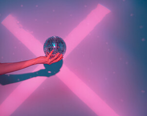 Close up of disco ball in female hand in cross shaped pink neon light in studio. Trendy poster to announce party