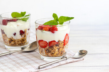 Homemade granola with slices of strawberries in transparent glasses on a light background....