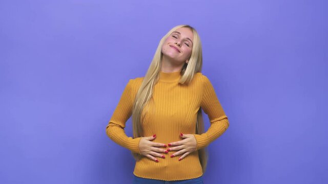 Young caucasian blonde woman touches tummy, smiles gently, eating and satisfaction concept