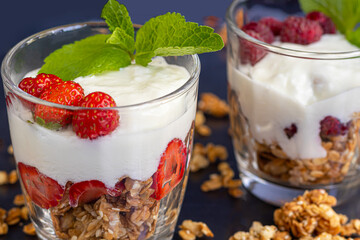 Homemade granola with slices of strawberries in transparent glasses on a dark background. Vegetarian dish. Healthy breakfast. Copy space.