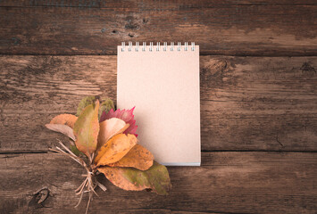 Naklejka na ściany i meble Notepad and autumn leaves on a natural wooden background. Autumn composition with a copy of the space. The concept of thanksgiving or Halloween.