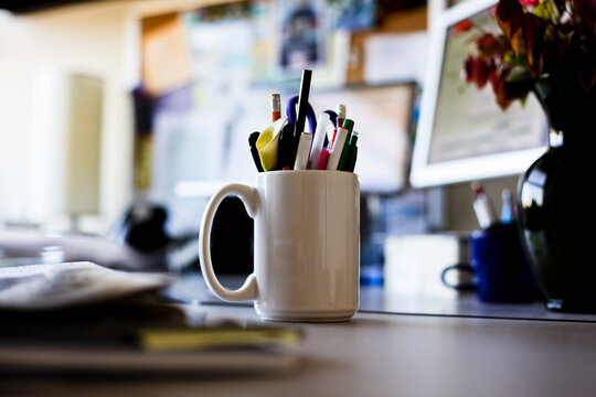 Mug full of writing instruments on a person's desk in an office