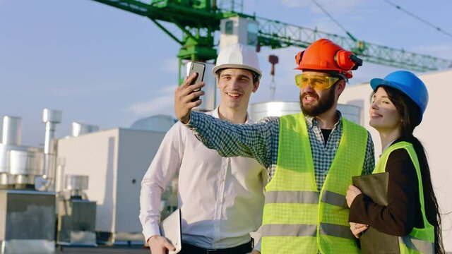 In front of the camera group of engineers and architect take some selfies on the top of construction site they smiling large and enjoying the time wearing safety helmets
