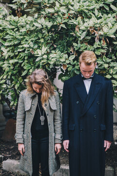 Young couple standing side by side in front of foliage