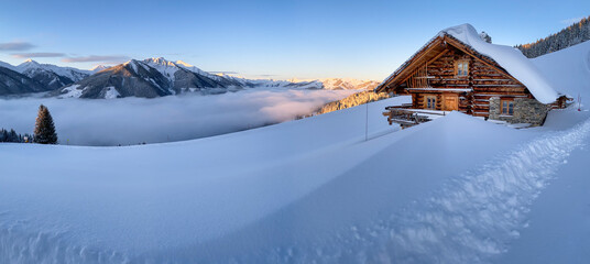 Snow covered mountain hut old farmhouse in the Austrian alps at sunrise against blue sky.