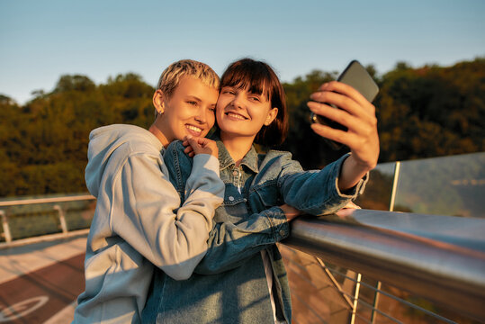 Happy together. Lesbian couple standing on the bridge and smiling while taking a selfie picture together