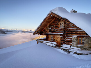 Snow covered mountain hut old farmhouse in the Austrian alps at sunrise against blue sky.