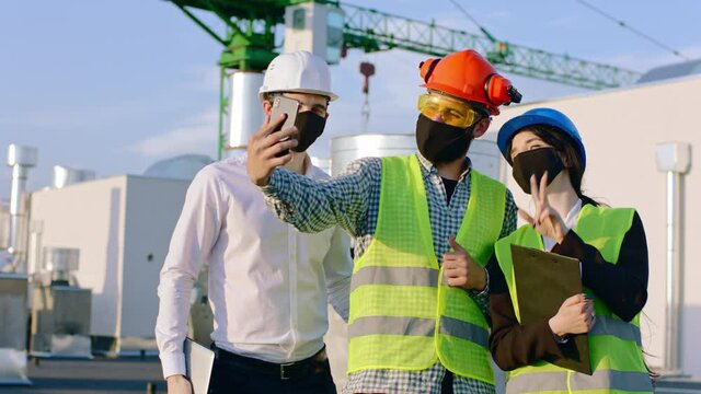 On the pandemic with coronavirus group of engineers and architect with protective mask on the top of construction site take some pictures using the smartphone they wearing safety helmets