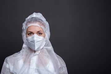 Portrait of young female doctor in a protective mask on a gray backgound. Medic in protective clothing looking away. A medic in protective clothing looks into the camera.