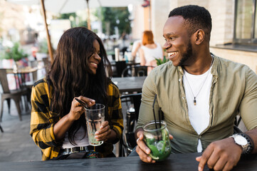 African American friends, young man and woman are sitting in a cafe drinking refreshing cocktails and having fun talking