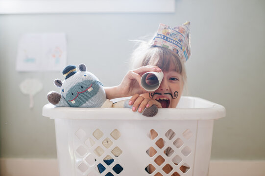 Child playing in laundry hamper with newspaper hat