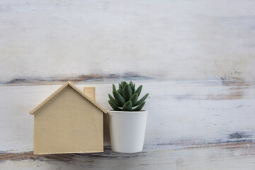 Business, Mortgage, Home Loan Concept. Closeup of wooden mini house toy with green plant pot on wooden table.