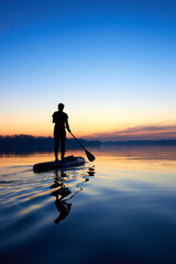 Silhouette of woman paddle on stand up paddle boarding (SUP) on quiet winter or autumn river at...