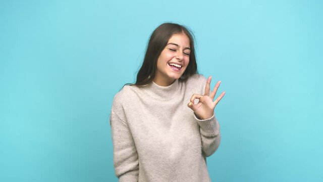 Young caucasian woman winks an eye and holds an okay gesture with hand