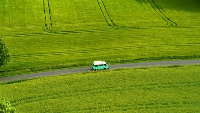 Mini bus driving on narrow country road, with green fields on both sides, drone stock footage 6