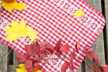 Autumn background, red tablecloth on a wooden table, yellow and red leaves