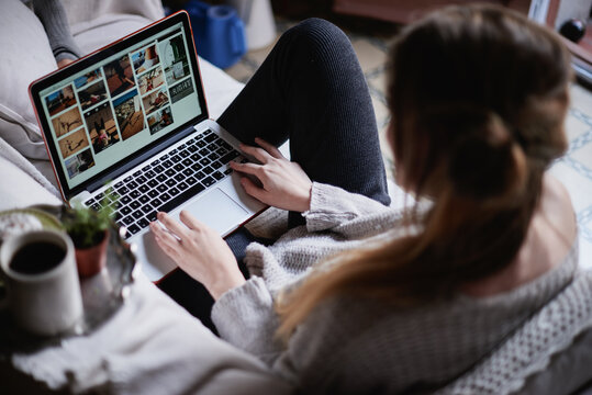Girl in gray sweater sitting on sofa and using laptop.