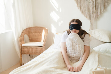 Young beautiful womanlying in comfortable bed and mask for sleep in the morning at cozy home. Self-isolation, stay home during quarantine, pandemic.