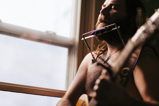 A soulful, scruffy musician plays guitar and harmonica