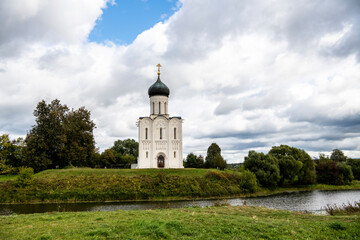 Fototapeta na wymiar snow-white stone old church against the background of a green meadow and lake before a summer thunderstorm