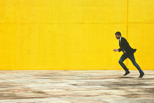 Businessman running on the street in front a yellow big wall.