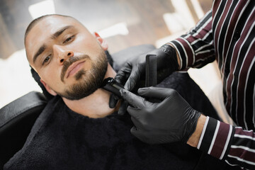 processes the beard shaving foam on the face, the client is a young man with dark hair. razor a...