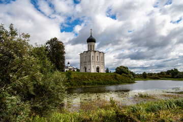 snow-white stone old church against the background of a green meadow and lake before a summer thunderstorm