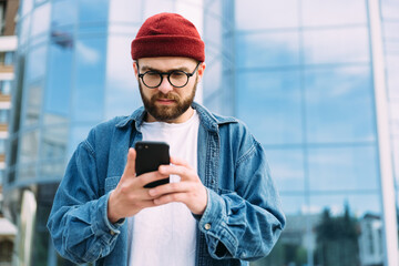 Serious handsome bearded male hipster looking at his smartphone and reading news
