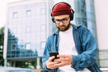 Young bearded hipster man in headphones using smartphone and having video chat.